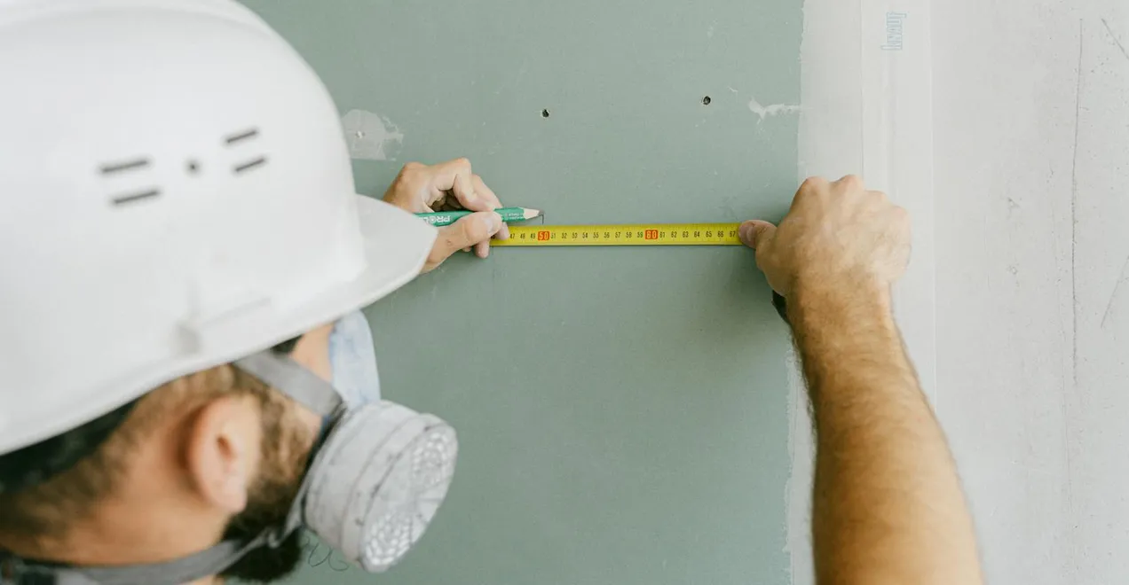 Measuring a wall with a tape measure during a job walkthrough.