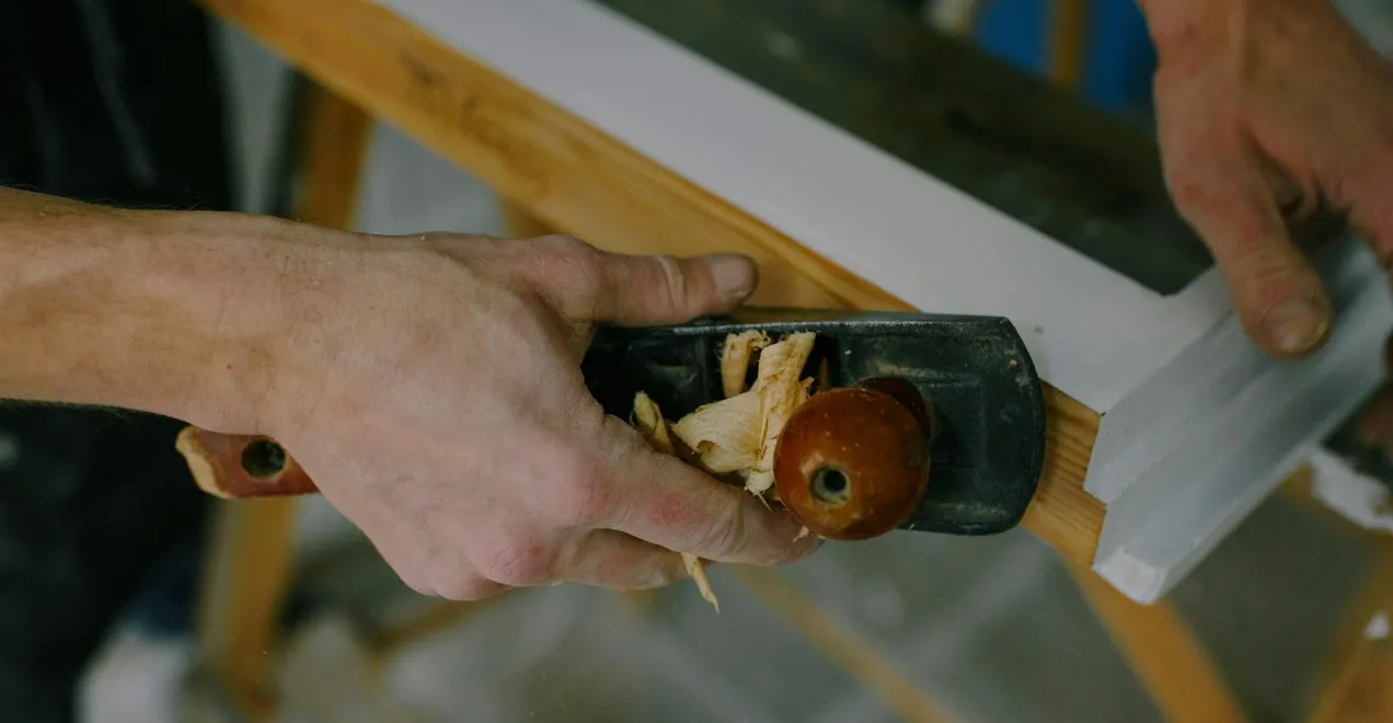 A carpenter finishing a wooden window frame with a hand plane.